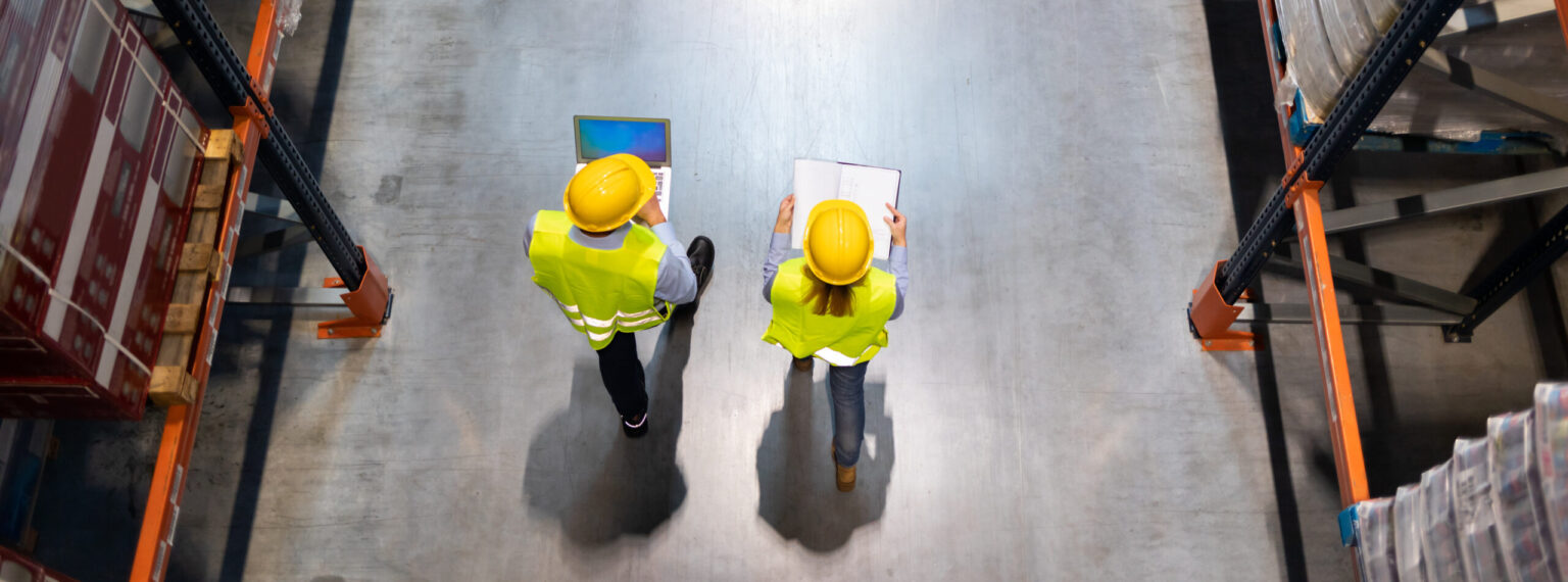 Warehouse workers consult delivery plans using laptop and electronic database
